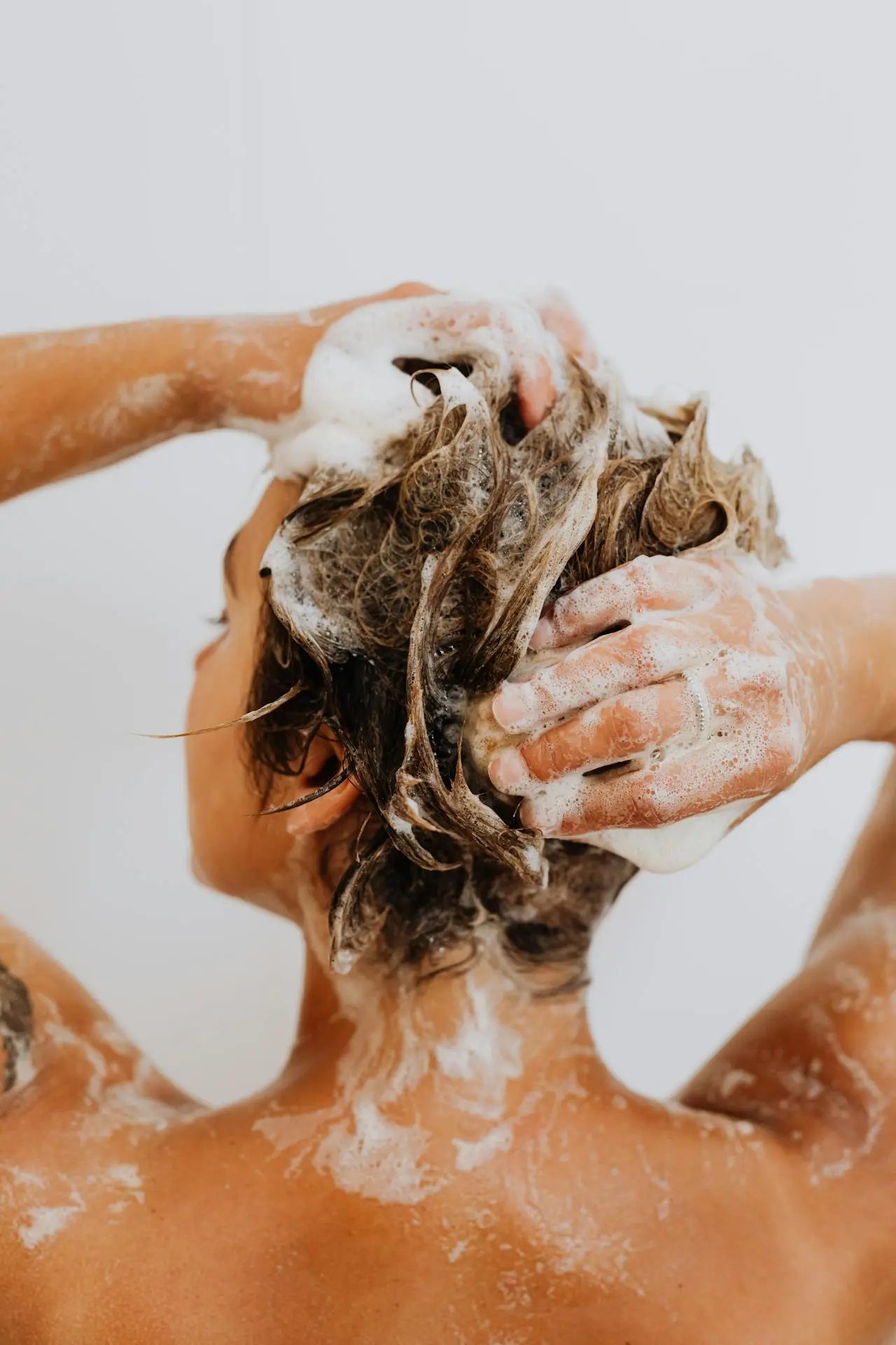 A woman washing her hair, head tilted back, lathering shampoo