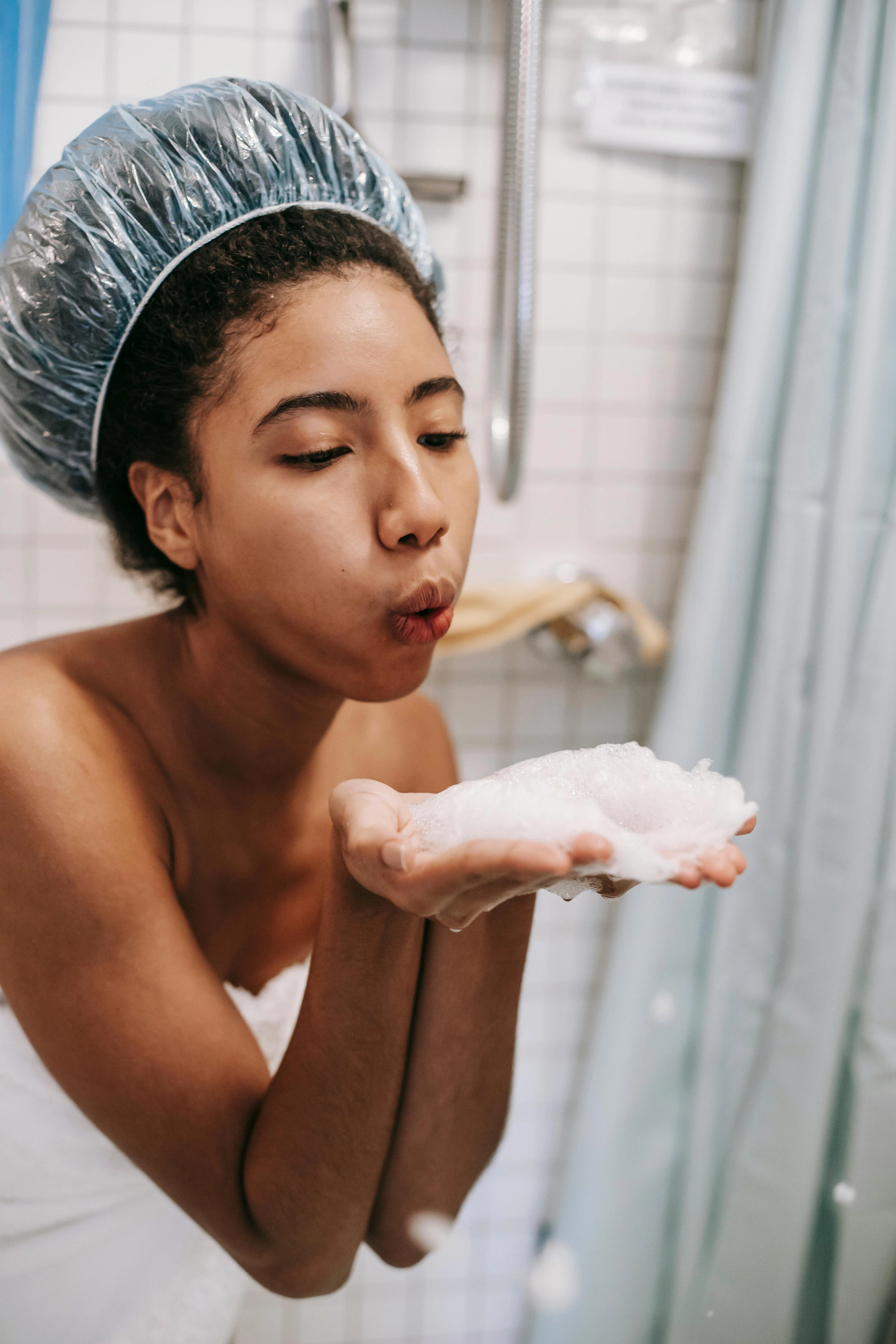 Woman in towel blowing on shampoo foam in hand